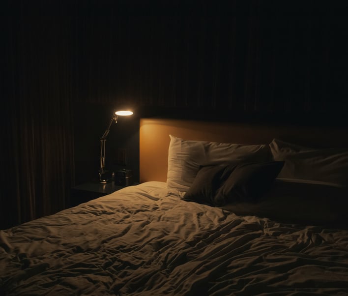 Chambre sombre, faiblement éclairée par une lampe de chevet, lit en désordre - symbolise l'atmosphère oppressante d'un cauchemar.