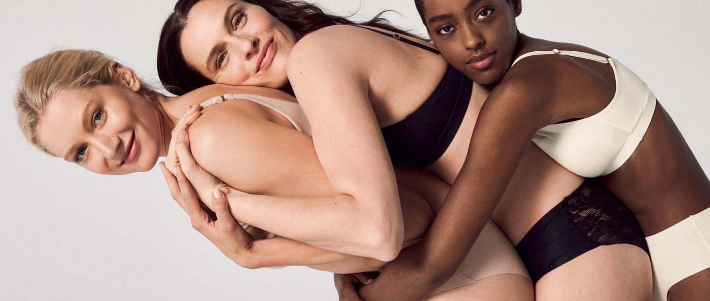 The picture shows three women hugging each other from behind. They are standing in front of a white background that emphasizes their tender embrace. The women are wearing CALIDA underwear, whose delicate fabrics gently caress their contours. The atmosphere radiates closeness and affection as the women lovingly snuggle together.