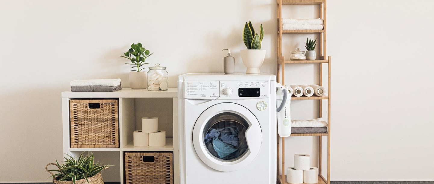 The picture shows a small section of a bathroom. You can see two shelves, a washing machine and neatly folded towels.