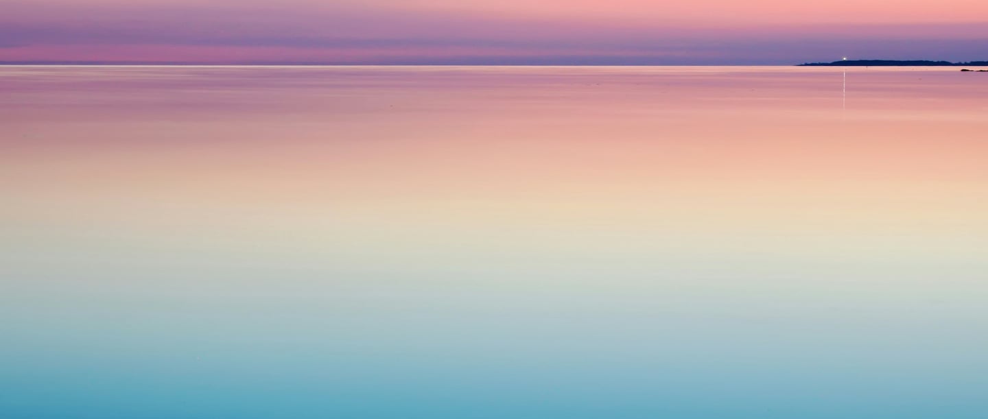 A calming sunrise over a tranquil ocean, with gentle colour transitions from blue to pink to light yellow, harmoniously blending the sky and the water.