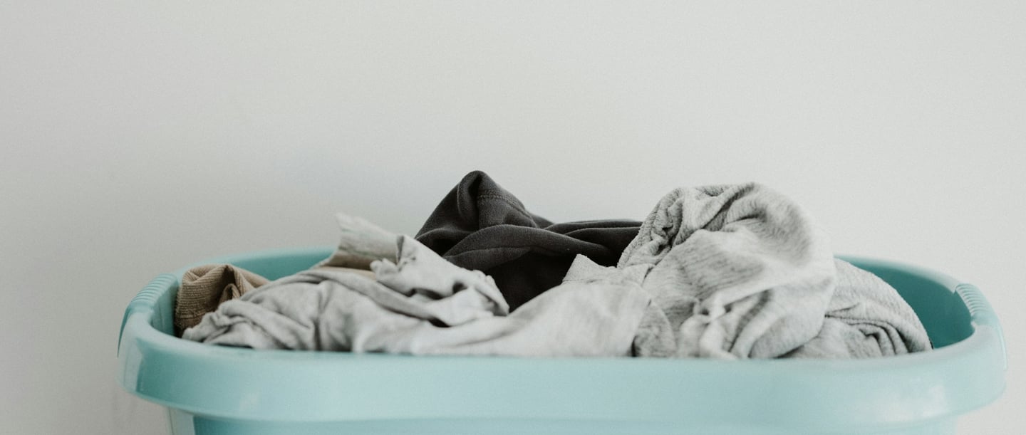 Un panier à linge turquoise rempli de vêtements de couleurs neutres.