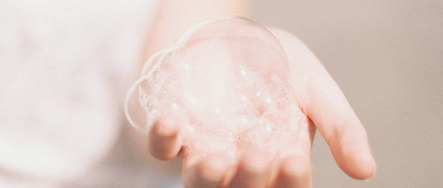 Mano con bolle di sapone, che simboleggia il lavaggio delicato a mano dei vestiti, ideale per i tessuti delicati.