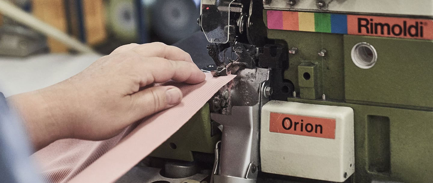 A person repairs small holes in clothing with a professional sewing machine in a workshop.