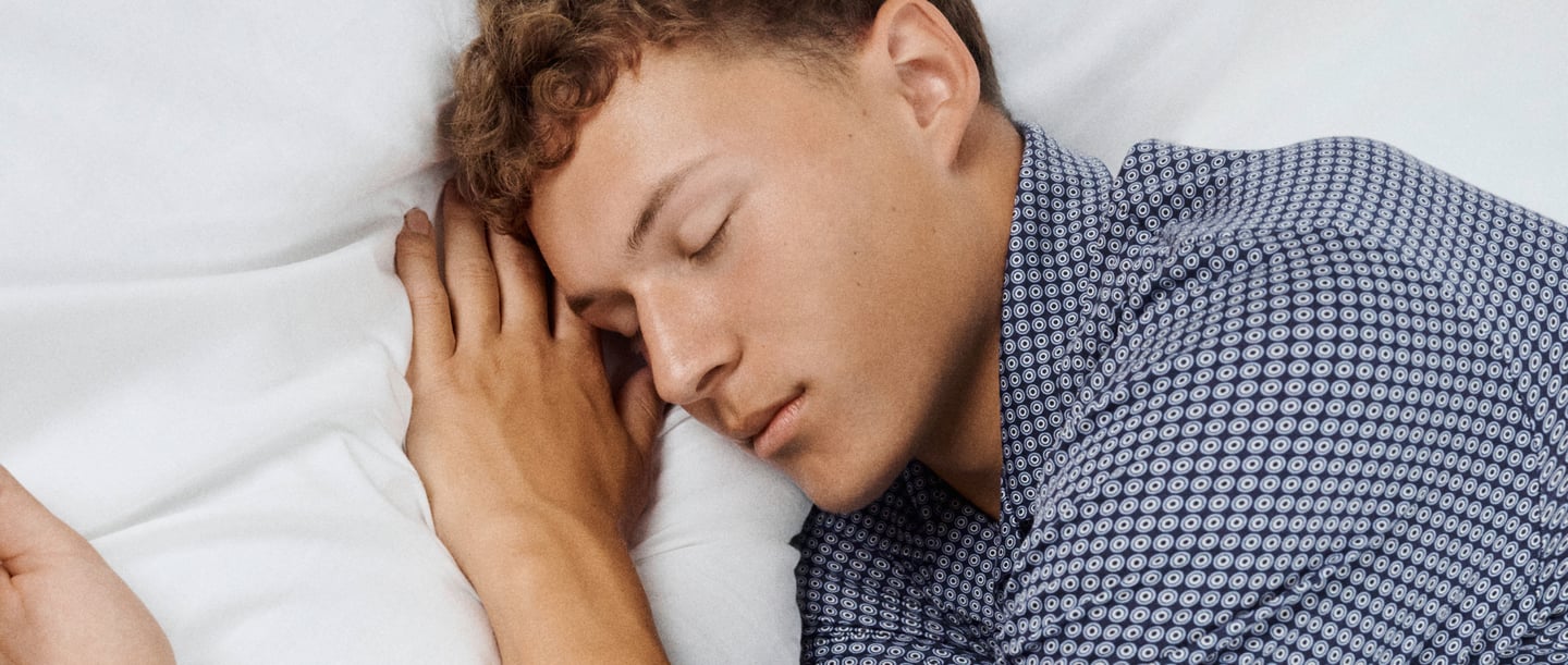 Un homme est allongé éveillé dans son lit, les yeux fermés, en accord avec la question : pourquoi ne puis-je pas dormir alors que je suis fatigué ?