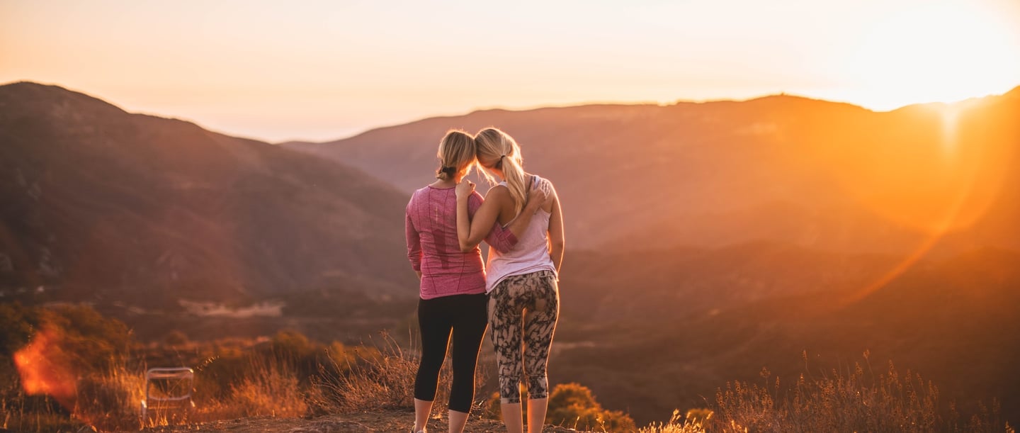2 Frauen auf einem Hügel schauen sich den Sonnenuntergang an.