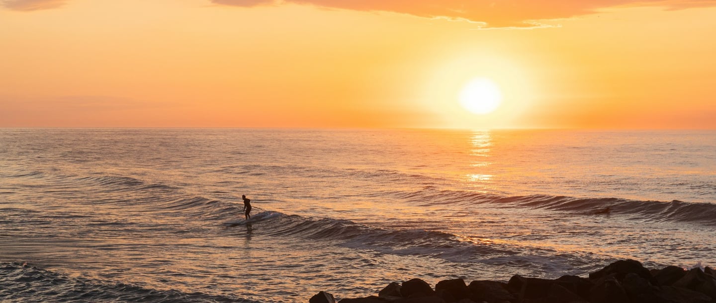 Tôt le matin sur la plage, une personne se tient debout dans la mer alors que le soleil se lève à peine.