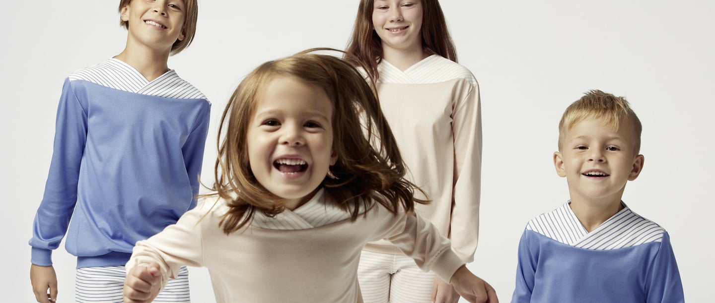 Quattro bambini in pigiama adatti alla loro età che guardano felicemente nella macchina fotografica simboleggiano il bisogno di dormire dei bambini e l'importanza di un abbigliamento da notte comodo per un sonno riposante.