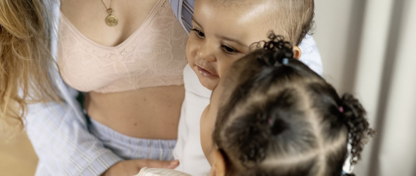 The mother wears the lace parfait pink coloured nursing bra without underwire. Over it she wears the light blue striped pyjama set from the Sweet Dreams series. Her two children are sitting on the mother's lap. 
