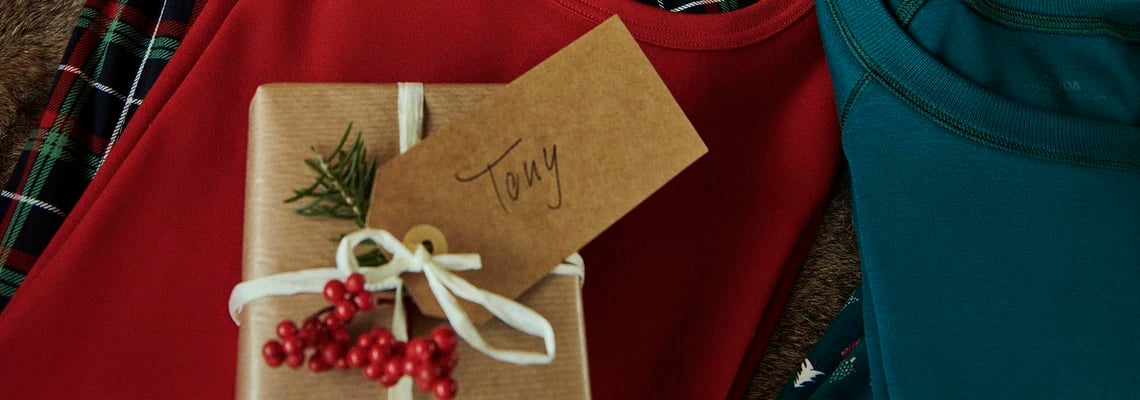Kleines verpacktes Geschenk mit dem Namensschild 'Tony'. Das Geschenk liegt auf Pyjamas von Calida.