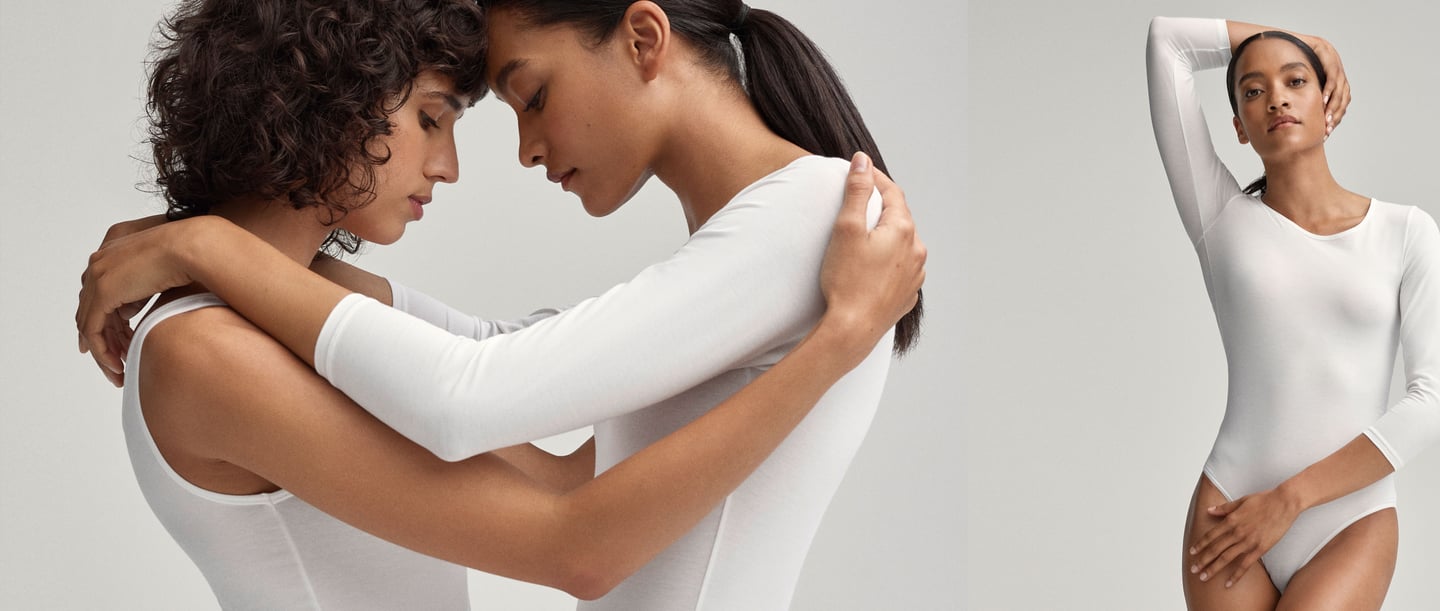 Two women embrace head to head on the left, while a woman on the right puts her arm around her head. They are all wearing a white bodysuit from CALIDA.