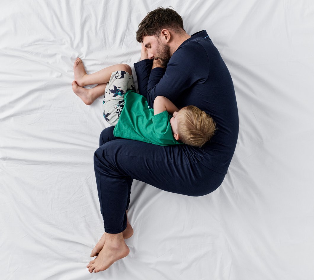 ein Mann und ein Kind liegen in Nachtwäsche bekleidet auf einer weißen Decke.