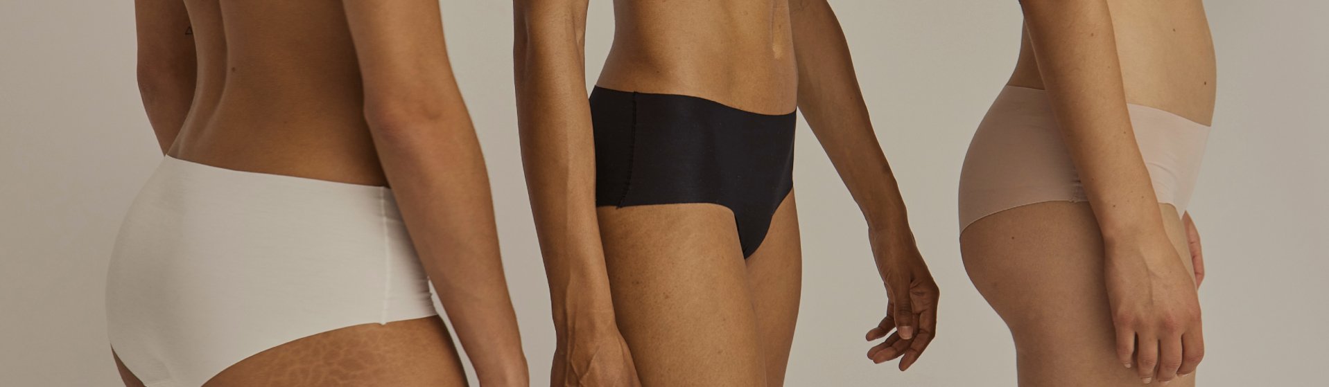 Drei Frauen von der Seite, bekleidet mit nahtlosen Slips in Weiß, Schwarz und Beige, vor neutralem Hintergrund.