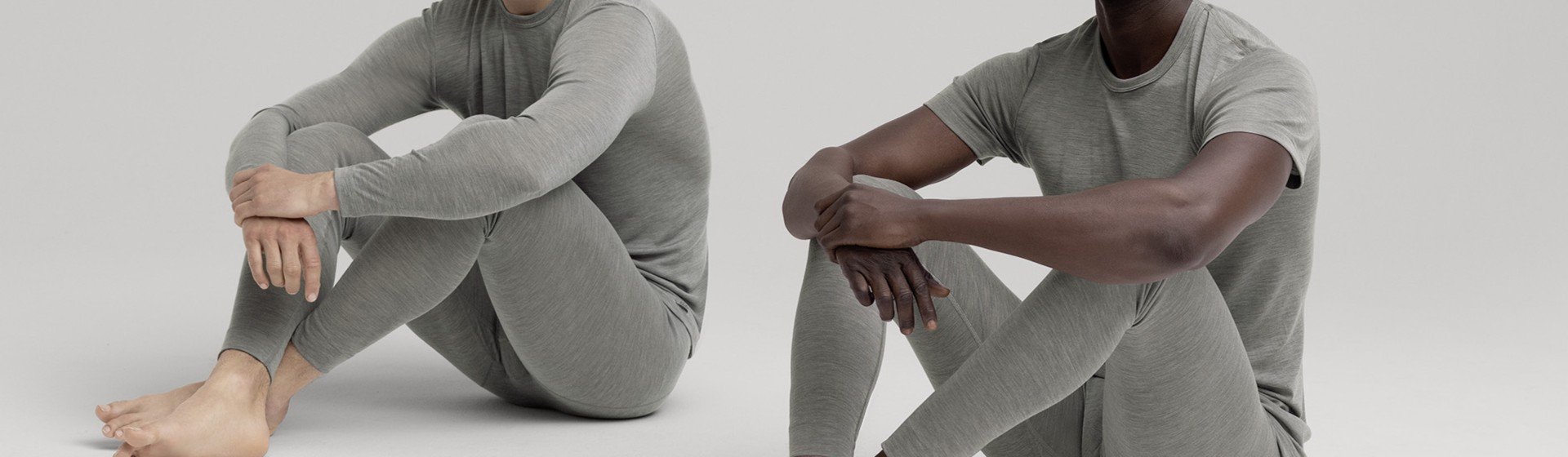 Zwei Männer sitzen barfuß auf dem Boden und tragen graue Langarm-Shirts und lange Unterhosen aus Wolle und Seide aus der CALIDA Serie 'Wool & Silk'.