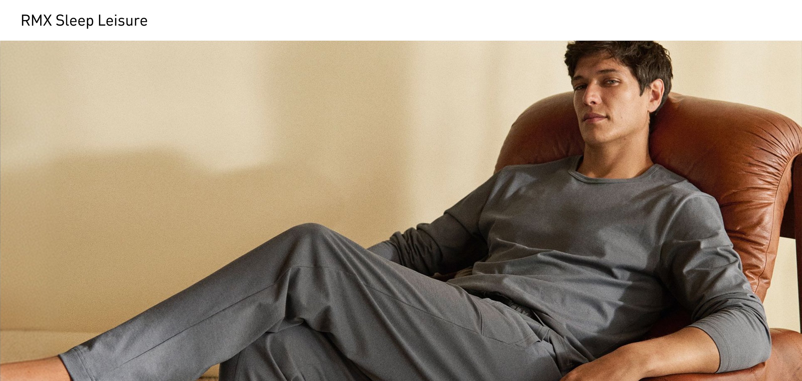 Ein Mann sitzt entspannt in einem Sessel und trägt ein graues Langarm-Shirt mit passender Pyjamahose mit Seitentaschen und Kordelzug aus der Serie RMX Sleep Leisure.