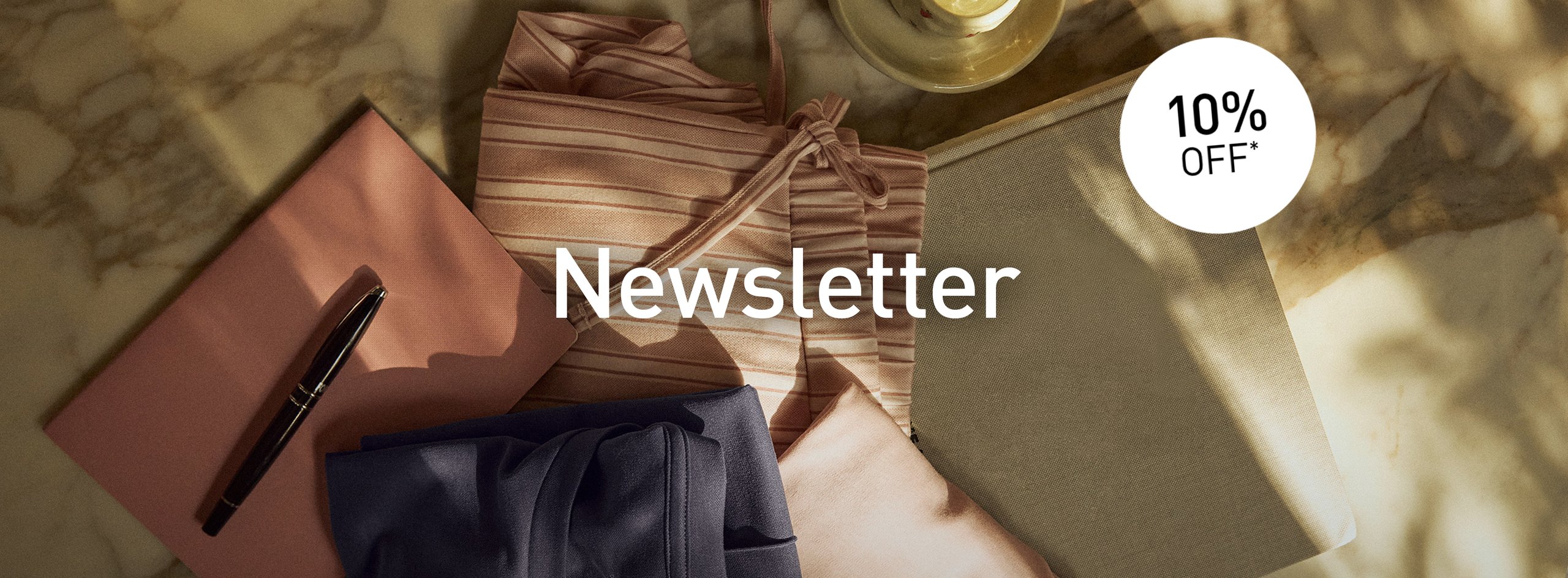 Folded loungewear and sleepwear styles in pink, blue, and natural tones on a marble table with newsletter notice and 10% discount.