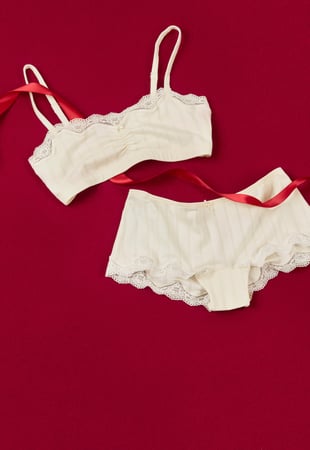 Bustier and shorty in cream with delicate lace details, decoratively staged with ribbon as a feminine gift idea.