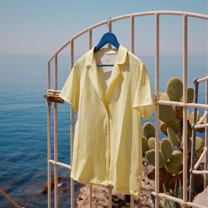 The image shows a yellow and white striped nightwear top in front of a seaside landscape.