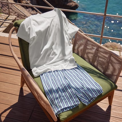 The image shows a white and blue nightwear set for men lying on an outdoor chair.