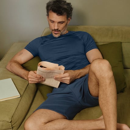 The image shows a man in a dark blue nightwear set on the sofa.
