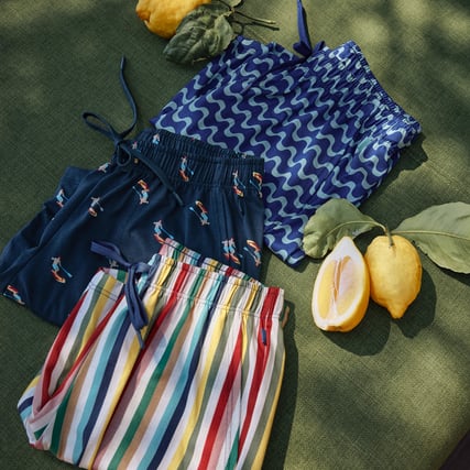 The image shows three pairs of colourful patterned men’s shorts in a summery setting.