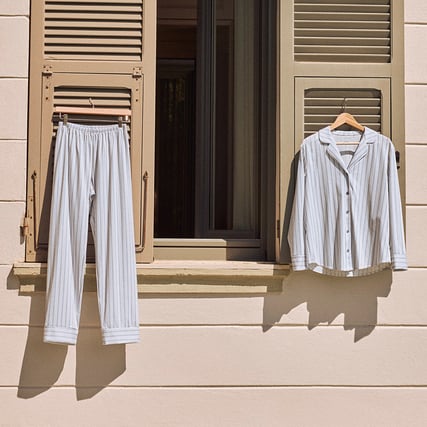 Das Bild zeigt ein weiß/blau gestreiftes Nachtwäsche Set hängend an 2 Fensterläden.