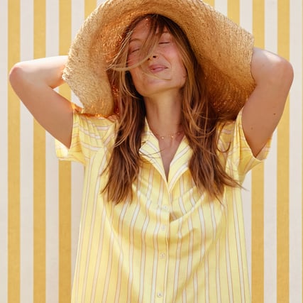 The female model is wearing a yellow striped pyjama top and is standing in front of a yellow striped background.