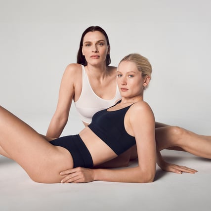 Una modella indossa un bustier bianco e l'altra modella indossa un bustier nero e uno slip della marca CALIDA della serie Elastic. 