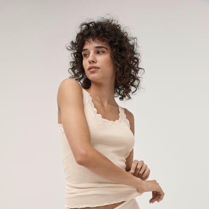 La modella indossa una canotta bianca della serie Richesse Lace del marchio CALIDA.