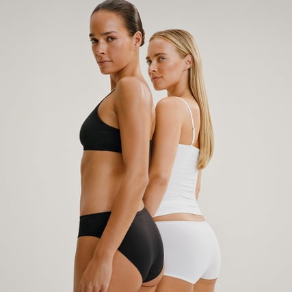 The model is wearing a black bustier and black high-waisted briefs from the Sleek Skin range by CALIDA.