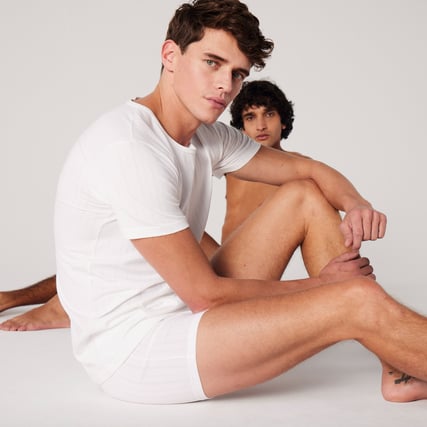 The model is wearing a white shirt and white boxer shorts from the Pure & Style range by CALIDA.