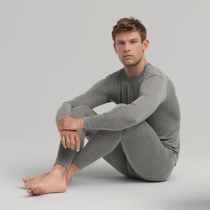 One model is wearing a grey long-sleeved shirt and grey trousers from the Wool & Silk range by CALIDA.