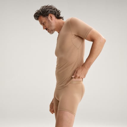 The model is wearing a beige shirt from the Natural Cooling range by CALIDA. 