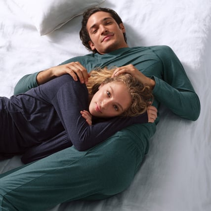 Das Bild zeigt ein weibliches Model, welches ein dunkelblaues Lounge-Set trägt, sowie ein männliches Model das ein dunkelgrünes Lounge-Set aus der Serie DSW Warming der Marke CALIDA trägt. 