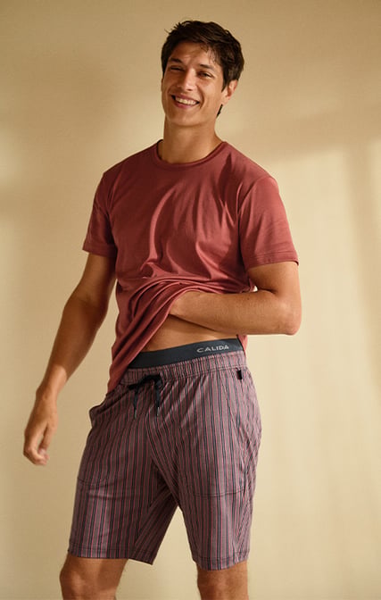 The man is wearing a short-sleeved T-shirt and matching Bermuda shorts with side pockets from the RMX Sleep Superlight range in brown. 