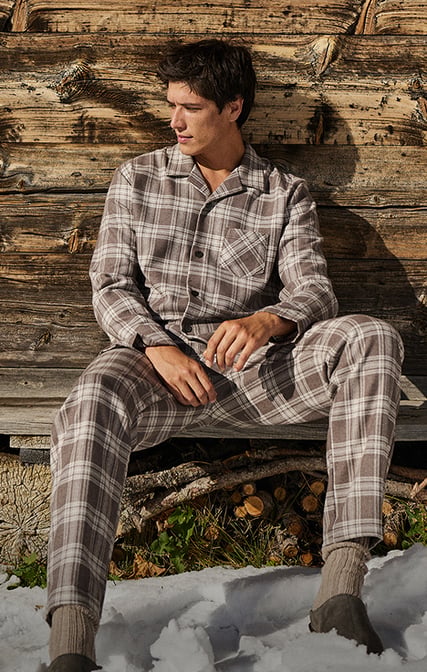 Das Model entspannt in einer gemütlichen Berghütte und trägt den durchgeknöpften Pyjama der Serie Relax Flannel Mood mit den passenden Socken für einen rundum komfortablen Look.