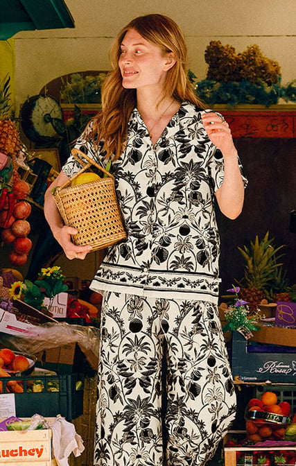 La signora fa shopping in tutta tranquillità al mercato; indossa una camicia a maniche corte con bottoni della linea Favourites Layering, abbinata ai pantaloni a 7/8 coordinati con una stampa moderna, per look mix-and-match eleganti