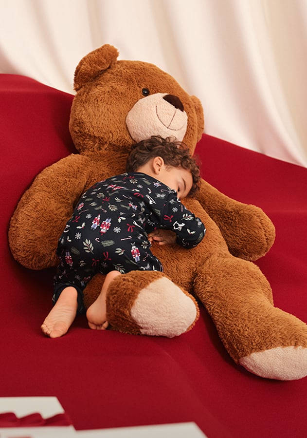 La photo montre un enfant en pyjama qui serre dans ses bras un gros ours en peluche.