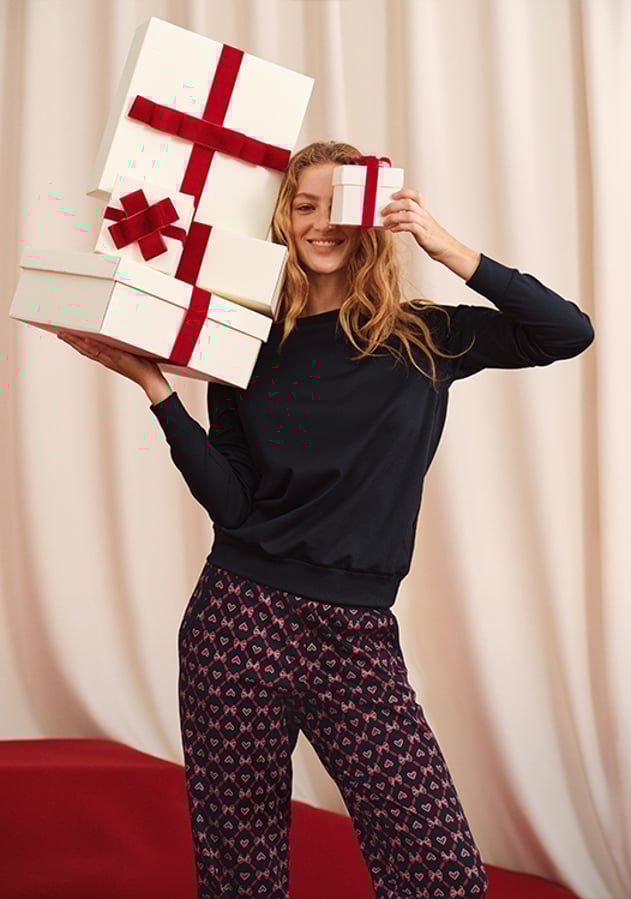La photo montre une femme en pyjama avec des cadeaux dans les mains.
