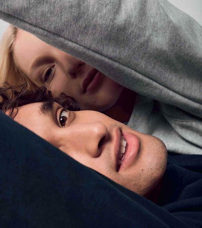 Two faces lying close together under gray fabric, intimate scene with soft light focused on closeness