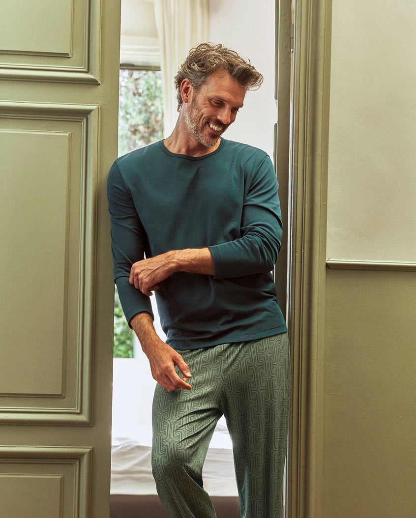 Ein männliches Model steht in einer Tür und trägt einen grünen Pyjama 