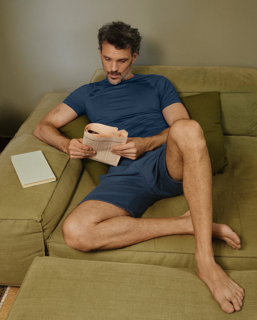 Homme se relaxant sur un canapé avec un journal, vêtu d'un ensemble homewear bleu de CALIDA