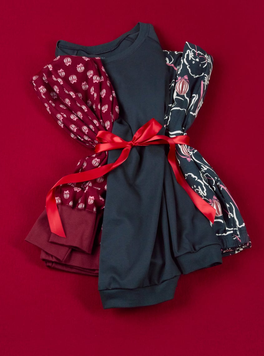 Folded nightwear with festive allover prints and decorative bow on a red background.