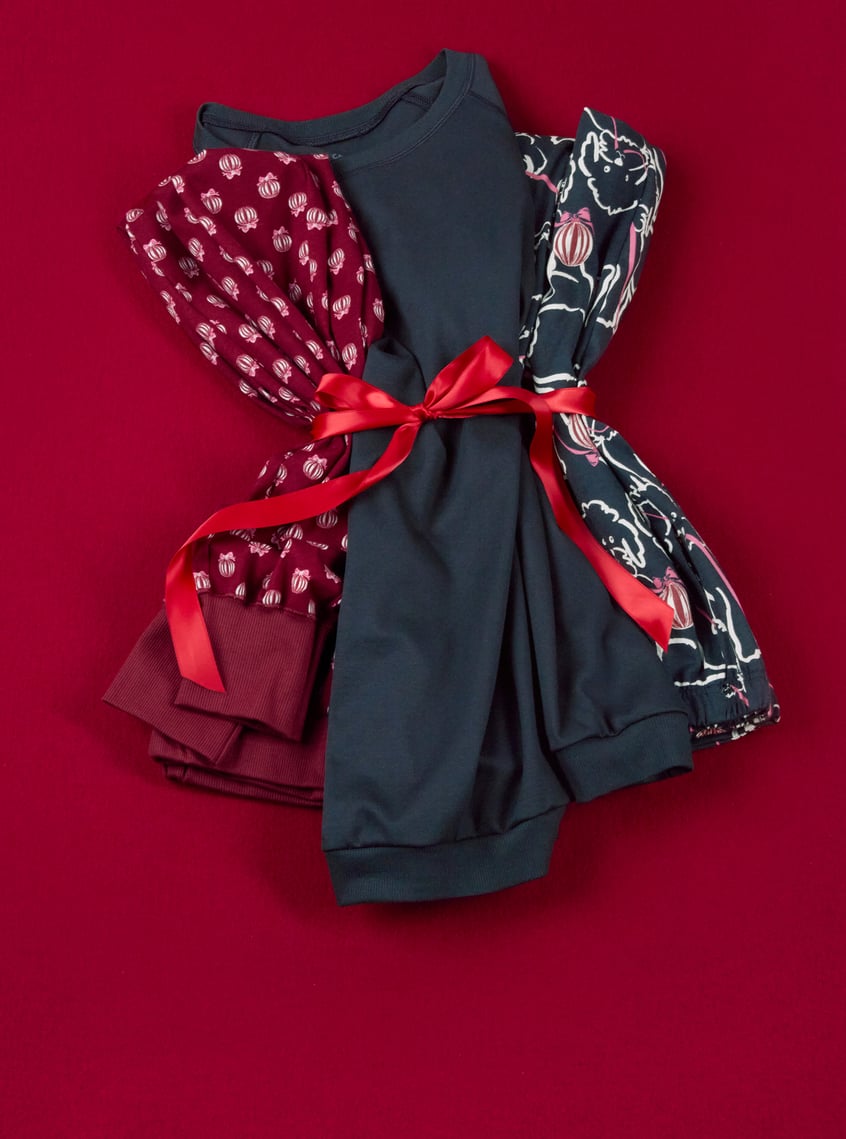 Folded nightwear with festive allover prints and decorative bow on a red background.