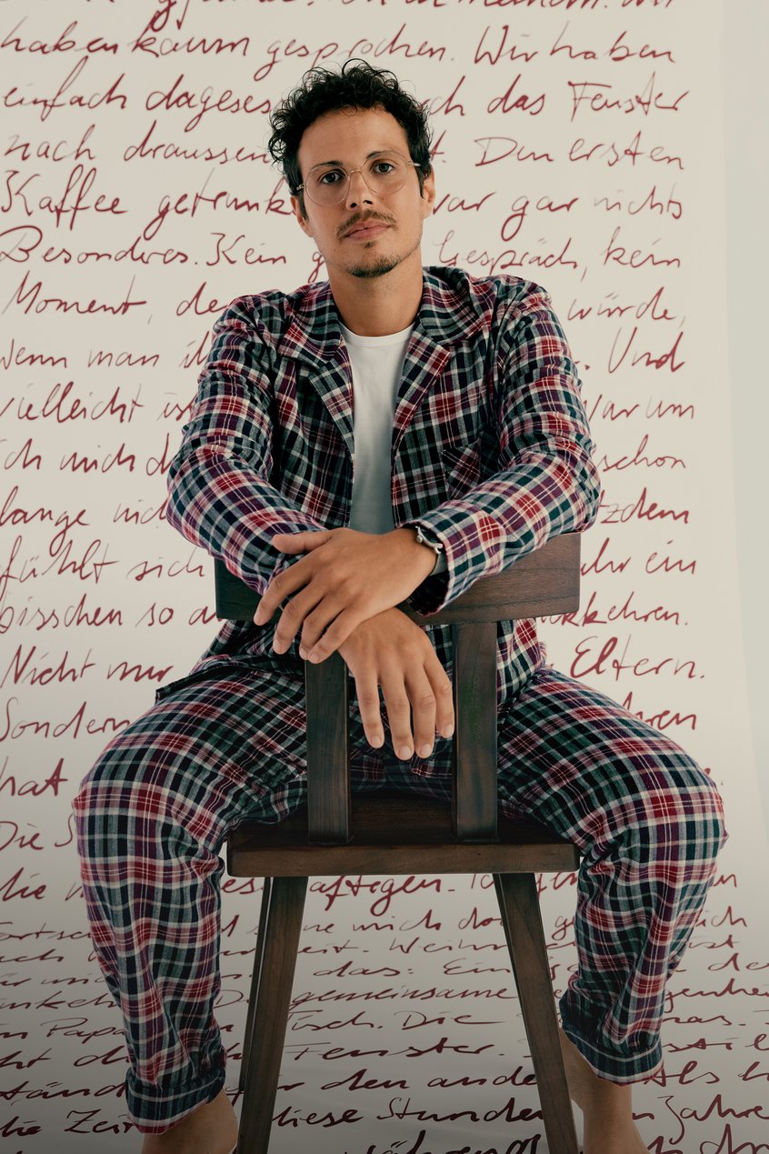 Mann in weihnachtlich karierten Flanell Pyjama vor einer Schriftrolle mit Weihnachts-Erinnerungen von CALIDA Kunden.
