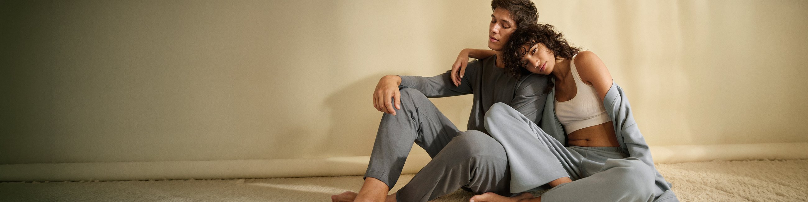 A woman and a man are lying on carpeted floor in nightwear from the HW26 collection.