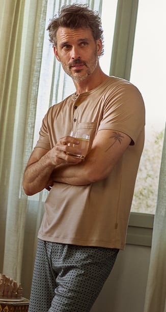 Ein männliches und ein weibliches Model liegen in einem Bett und tragen florale Pyjamas der Marke Calida in Pastelltönen.