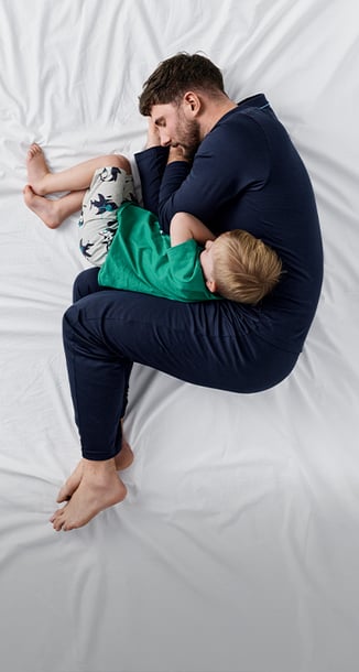 A man and a child, dressed in nightwear, are lying on a white blanket.