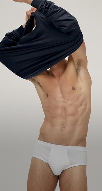 Auf dem Bild ist ein Mann in einem weißem Slip zu sehen, der sich das Oberteil über den Kopf auszieht.