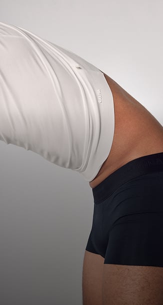 The picture shows a man pulling a T-shirt from the Clean Line range over his head.