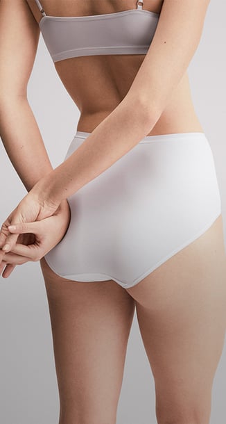 Die Dame steht entspannt und trägt ein Bustier mit dem passendem Slip der Serie Sleek Skin.
